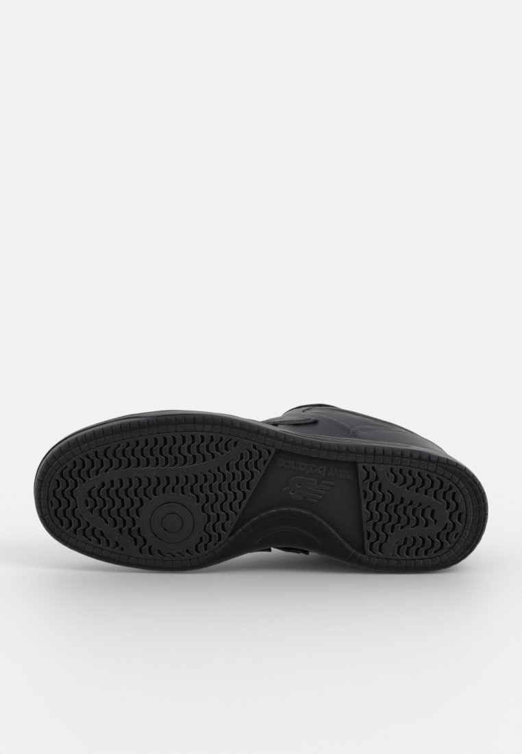 Semelle de chaussure de sport noire avec un caoutchouc texturé, présentant un motif de traction ondulé et un logo au centre. Conçue pour l'adhérence et la durabilité.