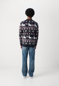 Suéter de malha azul marinha com padrões brancos de rena e flocos de neve, com um decote redondo e punhos canelados, combinado com jeans azul claro.