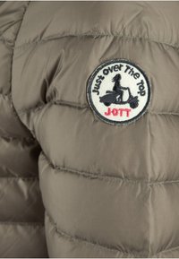Gewatteerde jas in gedempt grijs, met doorgestikte textuur. Voorzien van een ronde zwart-witte patch met de tekst "Just over The Top" en "JOTT".