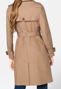 Trench beige con vita cinturata, dettagli con bottoni sulle spalle e spacco posteriore per facilitare i movimenti. Realizzato in un tessuto liscio e resistente.