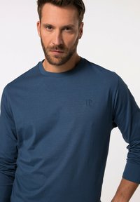 Camicia a maniche lunghe di colore blu realizzata in tessuto morbido, con scollatura rotonda e logo JP inciso in modo discreto sul lato sinistro del petto. Texture liscia.