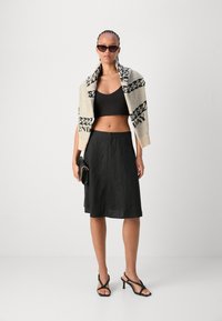 Sort cropped top, sort linned nederdel, creme strikket sjal med sort tekst, og sorte strophæle. Accessories inkluderer en lille sort clutch.