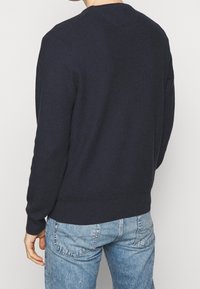 Marinblå stickad tröja med rund halsringning, långa ärmar och ribbstickade muddar och fåll. Slät textur, figursydd silhuett, inga synliga mönster eller detaljer.