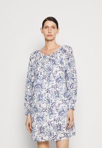 Blomstrete kjole laget av lett stoff, med hvit bunn og blå og lilla blomsterdesign, lange ermer og rynket halsutringning.