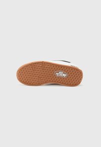 Vans sneakers med en gummi sål. Sålen er brun med et diamantmønster, har et logo og en hvid overdelen med sorte accenter.