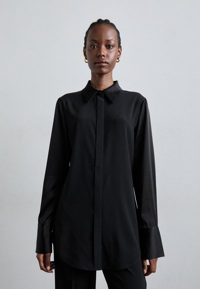 Sort langærmet skjorte med krave, der har knapper foran, glat stof og en let buet kant. Minimalistisk design med skræddersyet pasform.