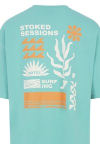 Světle modré tričko s bílými a oranžovými grafickými vzory, včetně vln, rostlin a textu "STOKED SESSIONS" a "PRTST SURFING."
