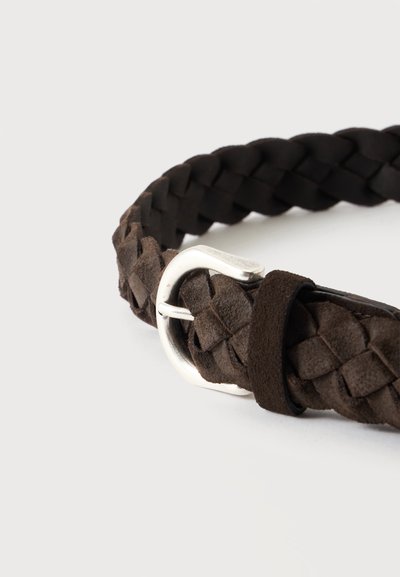 Gros plan d'une ceinture en cuir brun foncé tressée avec une boucle en métal argenté et une boucle en cuir sur fond blanc.