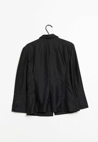 Svart kavaj hänger från en krok, med ett slätt, glänsande tyg, slagkrage och vida ärmar med ventildetalj bak.