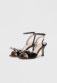 Czarne satynowe sandały na wysokim obcasie z odkrytymi palcami, kremowymi akcentami, paskiem wokół kostki i ozdobną kokardą. Charakteryzują się smukłym obcasem i metką z logo.