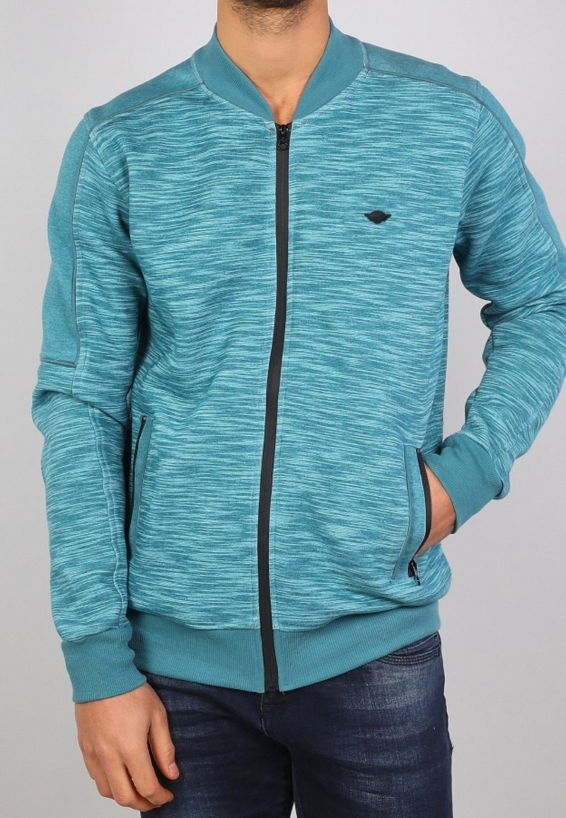 Veste bomber turquoise avec une surface texturée, des poignets côtelés et une fermeture éclair noire. Comprend deux poches latérales et un petit logo.