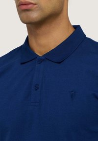 Polo shirt bleu marine en tissu coton, avec un col et une patte de boutonnage à deux boutons. Petit logo brodé sur le côté gauche.