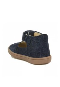 Chaussure en suède bleu marine avec des paillettes argentées, design à dos fermé, sangle Velcro et semelle en caoutchouc marron. Présente des découpes sur les côtés.