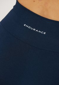 Tummansininen urheiluhousu, jossa on sileä kangas ja paksu vyötärönauha. "ENDURANCE" on printattu valkoisella ylävyöhykkeelle.