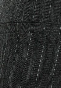 Schwarzer Fischgrätstoff mit vertikalen weißen Streifen, der eine glatte Textur und ein sauberes, strukturiertes Design aufweist; enthält ein Detail mit einer Gesäßtasche.