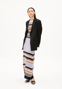 Zwarte blazer over een meerkleurige geribde knit top en gestreepte maxi rok. Getextureerde stof in grijs, roze, oranje en zwarte accenten. Zwarte sandalen.