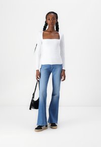 White long-sleeve top with a square neckline, paired with light blue flared jeans. Black bag and sneakers with white stripes accent the outfit.