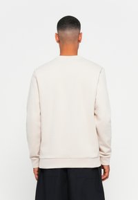 Sudadera beige claro con cuello redondo, mangas largas y puños acanalados. Material suave con una textura lisa, con un diseño simple.