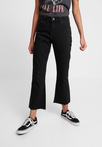 Černé džínové kalhoty s rozšířeným střihem, se surovými okraji a předními kapsami. V kombinaci s černobílými teniskami.