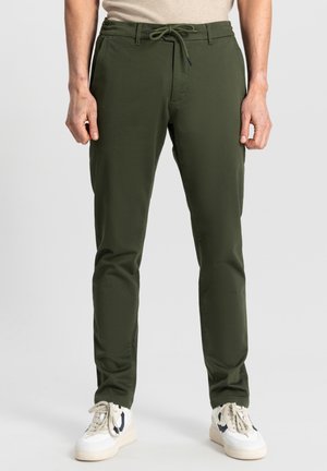 Dark green pants with a drawstring waist, slim fit design, smooth texture, and two side pockets, paired with white sneakers.
