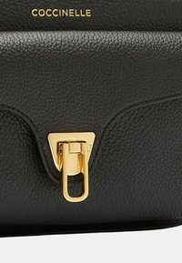 Borsa a tracolla in pelle nera strutturata con una chiusura triangolare in tonalità oro e branding impresso. Superficie texturizzata con accenti lisci.