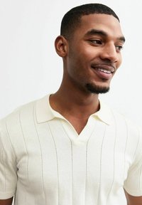 Polo crème à manches courtes avec un motif rayé texturé et un col en V, comportant des accents en tricot léger subtils à travers le textile.