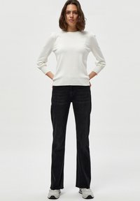 Suéter blanco de punto con mangas largas, puños y dobladillo acanalados, combinado con jeans negros slim-fit y zapatillas de color claro.