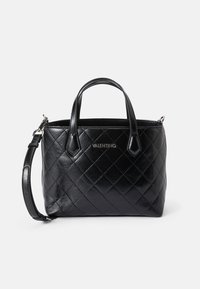 Bolsa de mão em pele preta com padrão acolchoado, alças superiores duplas e correia de ombro removível. Acessórios em prata com o logótipo da marca na frente.