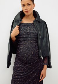 Veste en cuir noir à col montant, portée sur une robe à imprimé animalier sombre. La robe présente une silhouette ajustée et des fronces.