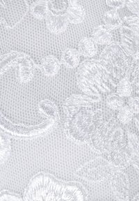 White embroidered fabric featuring floral designs, raised texture, and intricate detailing against a sheer background.