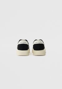 Svarte og beige sneakers med en overdel i semsket skinn og mesh, med en tykk såle og "Armani Exchange"-merke på hælen.