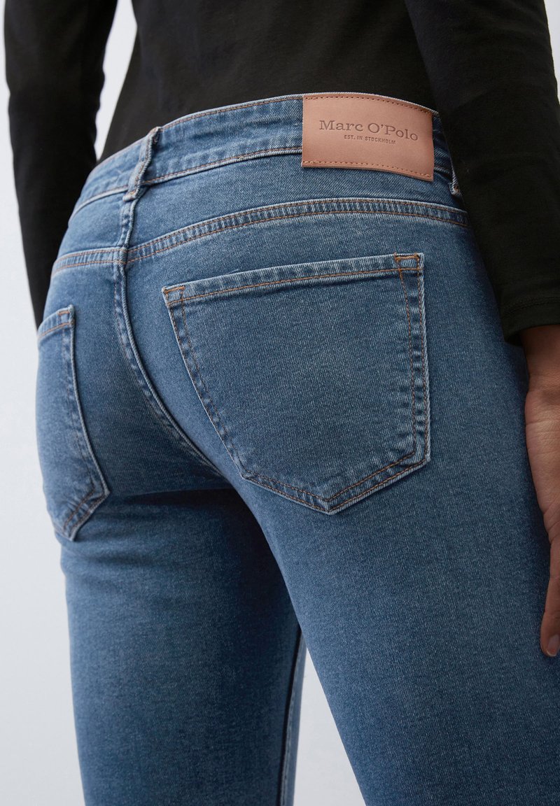 Niebieskie dżinsy o dopasowanym kroju, pięć kieszeni oraz brązowa skórzana naszywka z logo "Marc O’Polo" na tylnej części w talii.