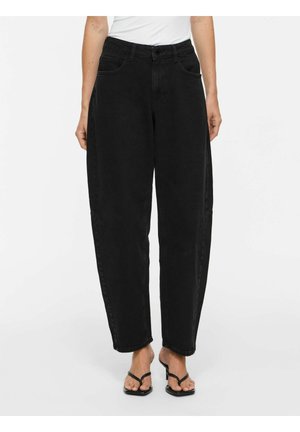 Kvinde iført sorte, løstsiddende jeans med høj talje og forlommer samt sorte hælsandaler mod en hvid baggrund.