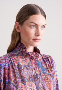 Bunte gemusterte Bluse mit Rüschekragen, verziert mit komplizierten Paisleymustern in den Farben Pink, Blau und Braun. Knopfleiste vorne.