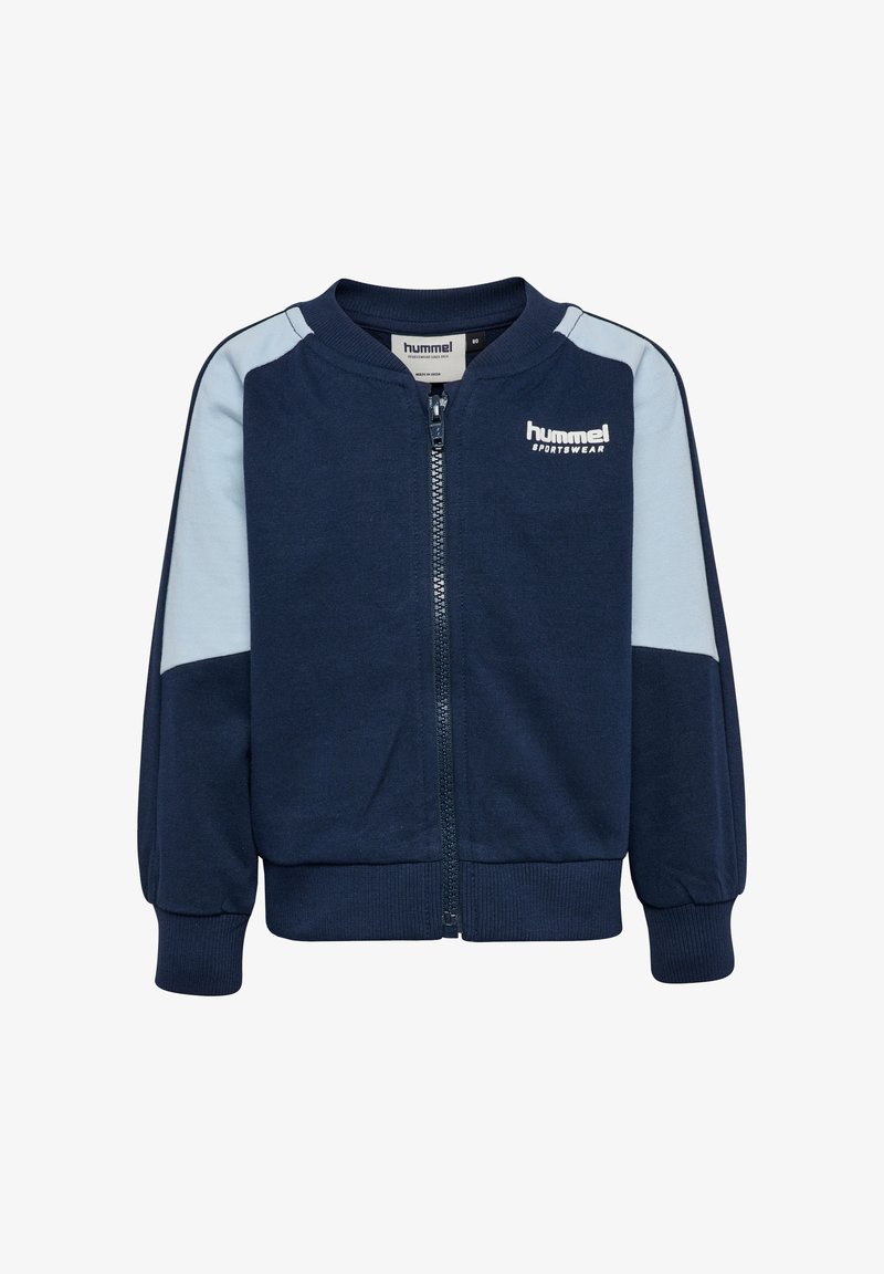 Granatowa kurtka na zamek z jasnoniebieskimi panelami, ściągaczami na mankietach i u dołu. Na górnej lewej stronie znajduje się biały znak "hummel". Miękki materiał.