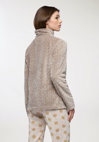 Giacca in pile marrone chiaro con colletto alto e texture a zigzag, abbinata a pantaloni crema con stampa di orsi in colori tenui.