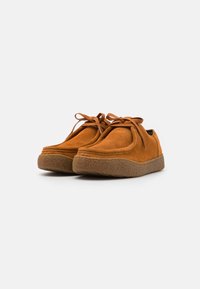 Scarpe in camoscio marroni con punta tonda, dotate di una suola in gomma spessa e testurizzata e lacci abbinati. Design morbido e imbottito.