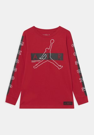 T-shirt Jordan à manches longues rouge avec silhouette Jumpman blanche et texte noir "AIR" sur la poitrine, texte "JORDAN" sur les deux manches.