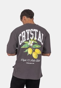 Šedé oversize tričko s výrazným bílým nápisem "CRYSTAL" a barevnou grafikou citronu na zadní straně, doplněné květinovým vzorem.