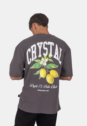 Szara, oversize'owa koszulka z wyrazistym, białym napisem "CRYSTAL" oraz kolorową grafiką cytryny na plecach, do której dołączony jest kwiatowy wzór.