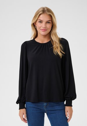 Maglia nera a maniche lunghe con scollatura arricciata e maniche a palloncino, caratterizzata da polsini testurizzati e una vestibilità ampia. Abbinata a jeans blu.