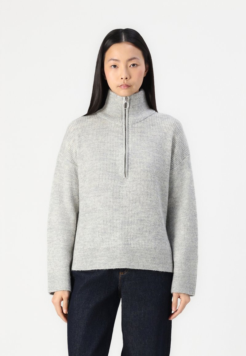 Jasnoszary sweter z dzianiny z wysokim kołnierzem i półzamkiem. Posiada długie rękawy oraz luźny krój, wykonany z teksturowanej przędzy.