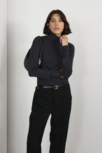 Un haut col roulé noir en matière côtelée, associé �à un pantalon noir taille haute. Le mannequin porte un petit sac noir.