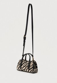 Sac à main imprimé zèbre avec accents en cuir noir, forme structurée, doubles poignées supérieures et bandoulière amovible. Détail de fermeture éclair dorée.
