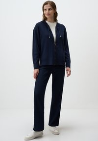 Felpa navy con zip, cappuccio e due tasche frontali, abbinata a pantaloni navy con texture e sneakers bianche, il tutto in un fit casual.