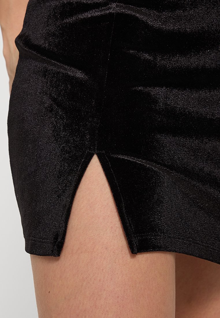 Czarna aksamitna mini spódnica z bocznym rozcięciem, gładką teksturą i dopasowanym krojem. Odbijająca powierzchnia podkreśla jej elegancki wygląd.