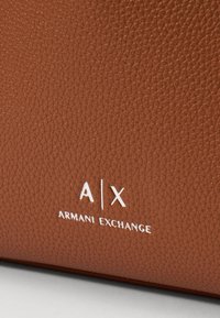 Smeđi teksturirani kožasto materijal, s istaknutim A|X i ARMANI EXCHANGE oznakama u bijeloj boji. Glatka površina s strukturiranim dizajnom.