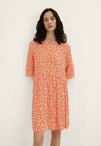 Robes fleuries orange à manches courtes, avec un décolleté boutonnière et une coupe ample. Le motif présente de petites fleurs blanches sur un tissu texturé.