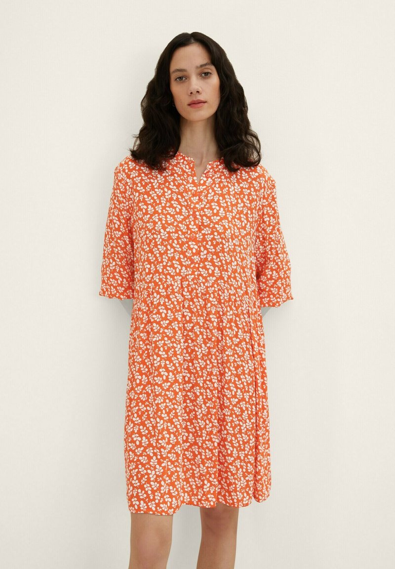 Robes fleuries orange à manches courtes, avec un décolleté boutonnière et une coupe ample. Le motif présente de petites fleurs blanches sur un tissu texturé.