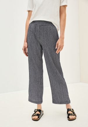 Grå strukturerade vida byxor med elastisk midja, i kombination med svarta sandaler med guldspännen. Enkelt, avslappnat design.
